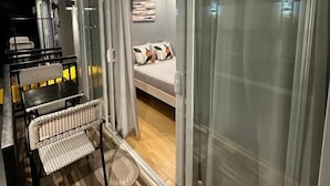 Una habitación moderna con una cama, un área de comedor con sillas y un amplio ventanal corredizo que da a un balcón.