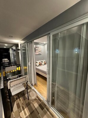 A modern room with a bed, a dining area with chairs, and a large sliding glass door leading to a balcony.