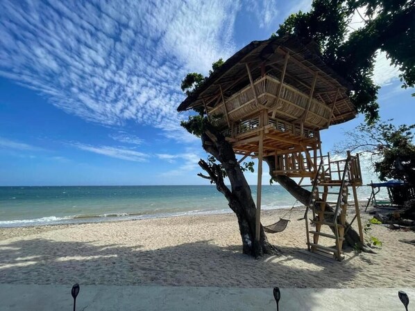 A beach with a wooden structure supported by a tree, a hammock, and a clear sky.