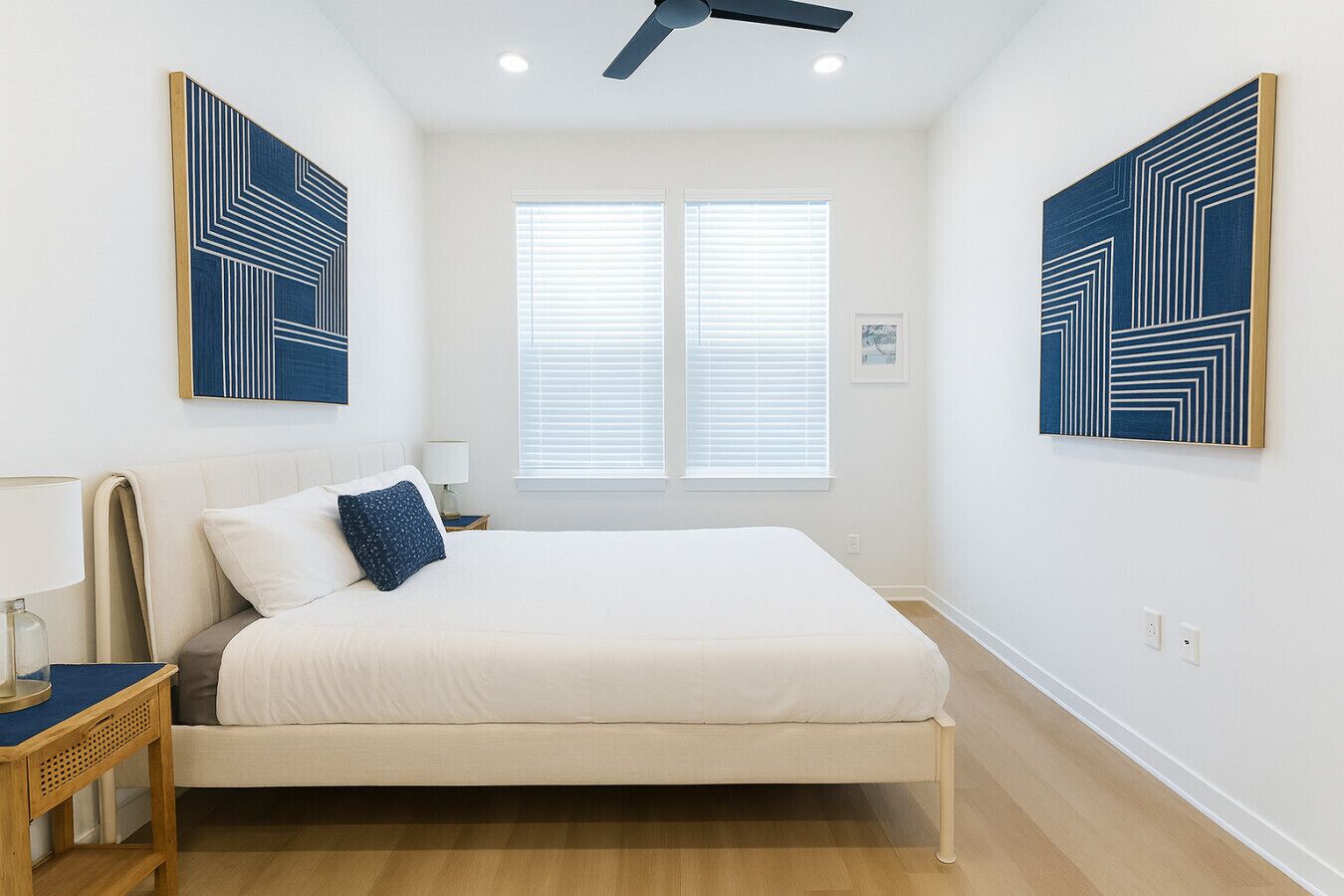 Un dormitorio con cama, mesita de noche, lámpara y dos ventanas con persianas.