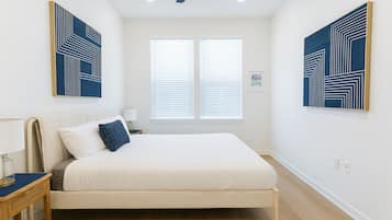 Un dormitorio con cama, mesita de noche, lámpara y dos ventanas con persianas.