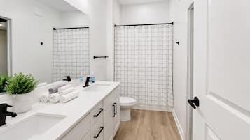 Un baño moderno con lavamanos, espejo y retrete blancos, una ducha con cortina de diseño de cuadrícula y suelo de madera.