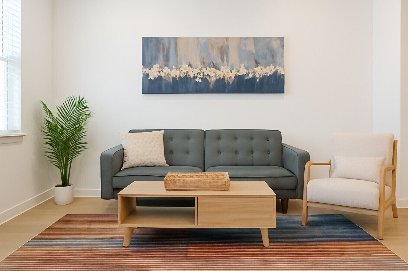 A modern living room with a grey sofa, a wooden coffee table, a white armchair, and a large abstract painting on the wall.
