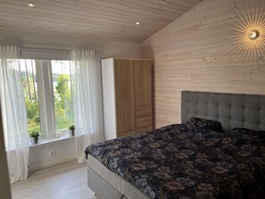 Une chambre à coucher avec un lit, une armoire, une fenêtre avec des rideaux et une vue sur la verdure à l’extérieur.