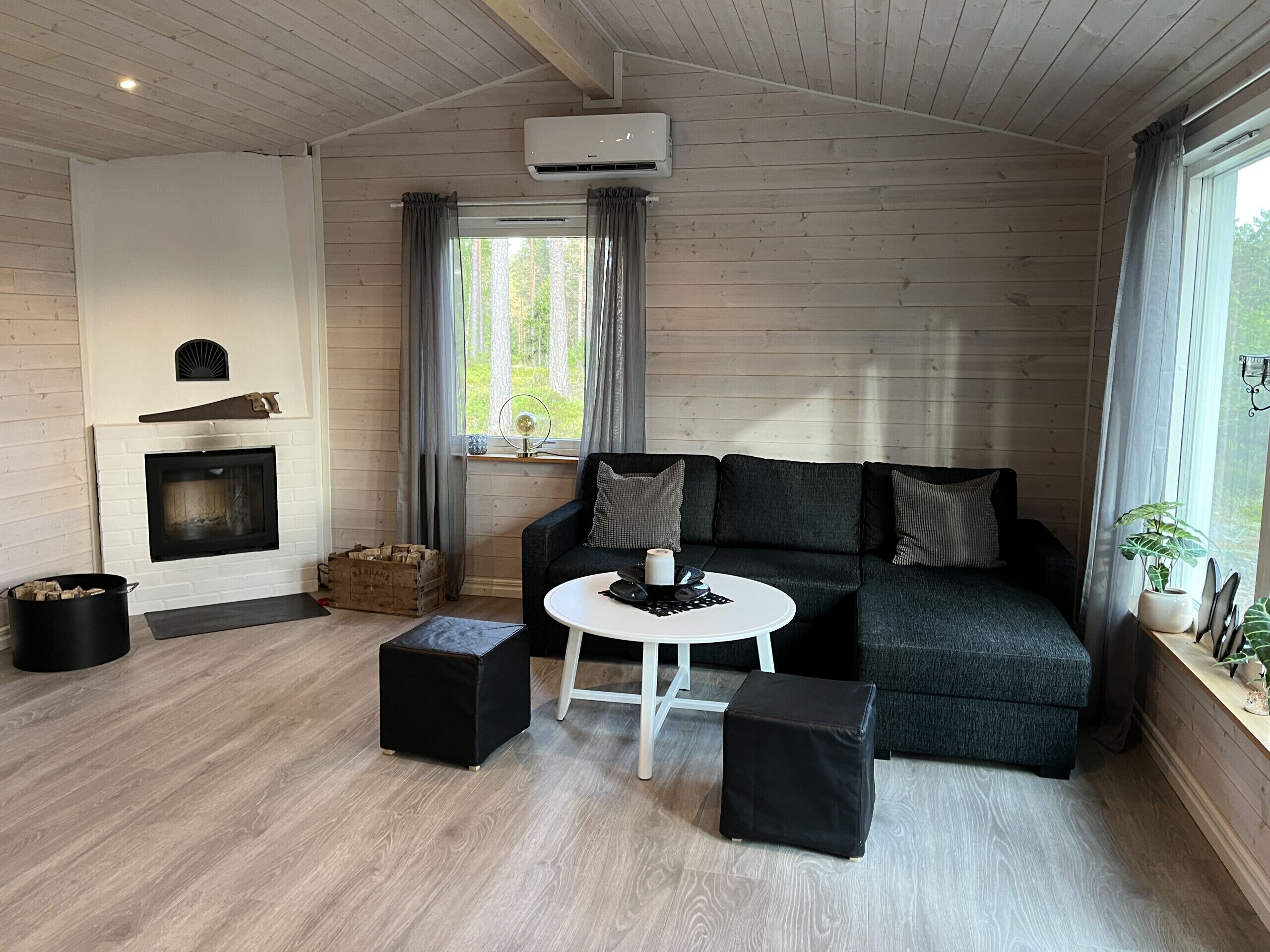 A cozy living room with a fireplace, a sofa, a coffee table, and a window with curtains.