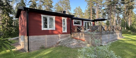 En rød hytte med terrasse, omgivet af træer.