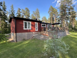 Une cabane rouge dotée d’une terrasse, entourée d’arbres.