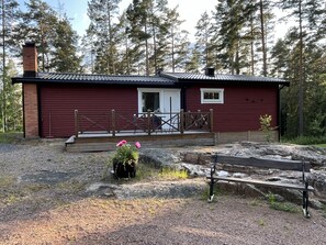 Une cabane rouge avec une terrasse en bois, une porte et une petite fenêtre.