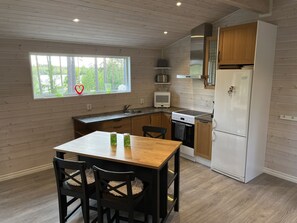 Eine kompakte Küche mit Holzschränken, einem weißen Kühlschrank, einem eingebauten Backofen und einem Fenster mit Blick auf Bäume.