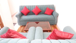 A grey sofa with red cushions and a glass coffee table in a well-lit room.