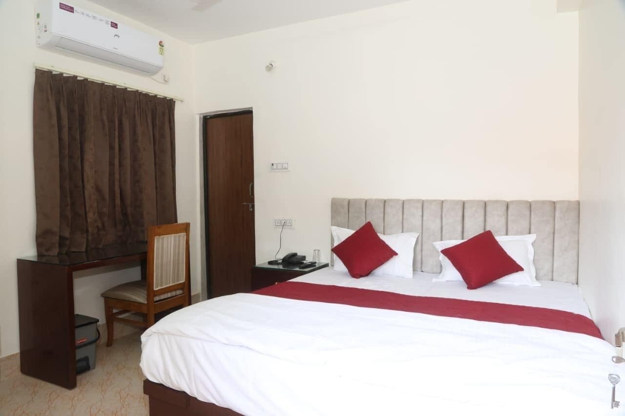 A hotel room with a bed, a desk with a chair, a telephone, and an air conditioning unit.