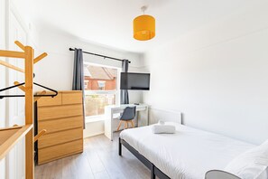 Ein modernes Schlafzimmer mit Bett, Schreibtisch, Stuhl, Fernseher und einem Fenster mit Vorhängen.