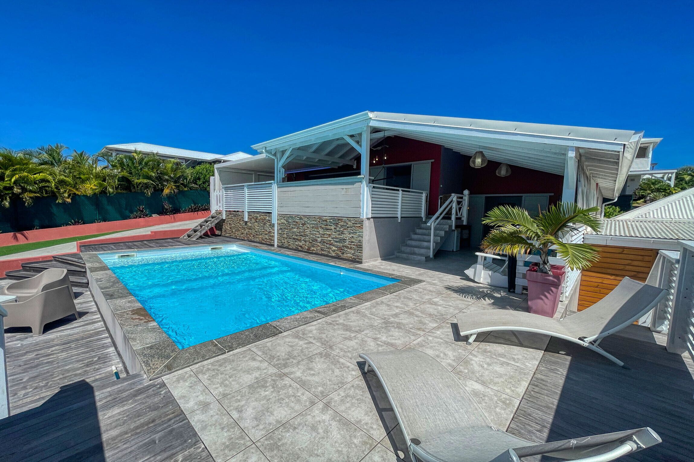 A rooftop pool area with a clear blue pool, a covered seating area, and a stone wall.