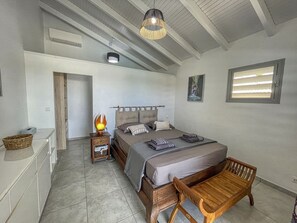 A bedroom with a bed, bedside table, lamp, window, and a wooden bench. - Villa with Bungalow & Pool – Sleeps 10 (Saint-François)