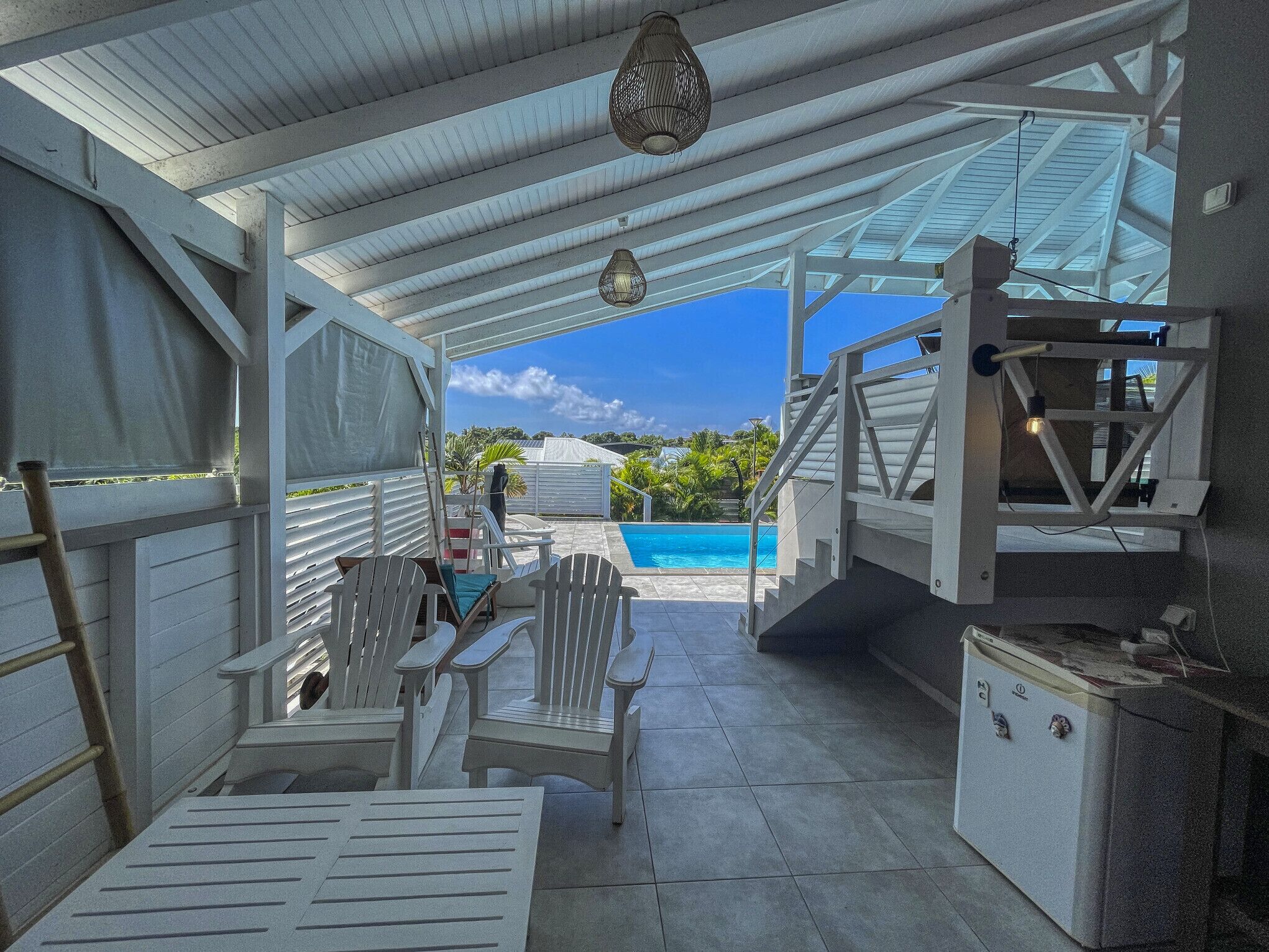 Un espace extérieur abrité avec une piscine, des meubles blancs et une échelle.