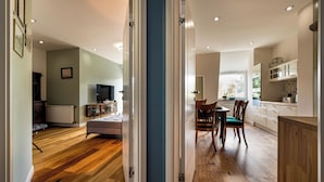 Un interior moderno con suelo de madera, una zona de comedor con sillas, una cocina con armarios y un televisor en la sala.