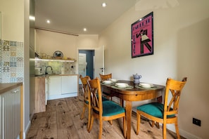 Un comedor con mesa y sillas de madera, una cocina al fondo y un cartel en la pared.