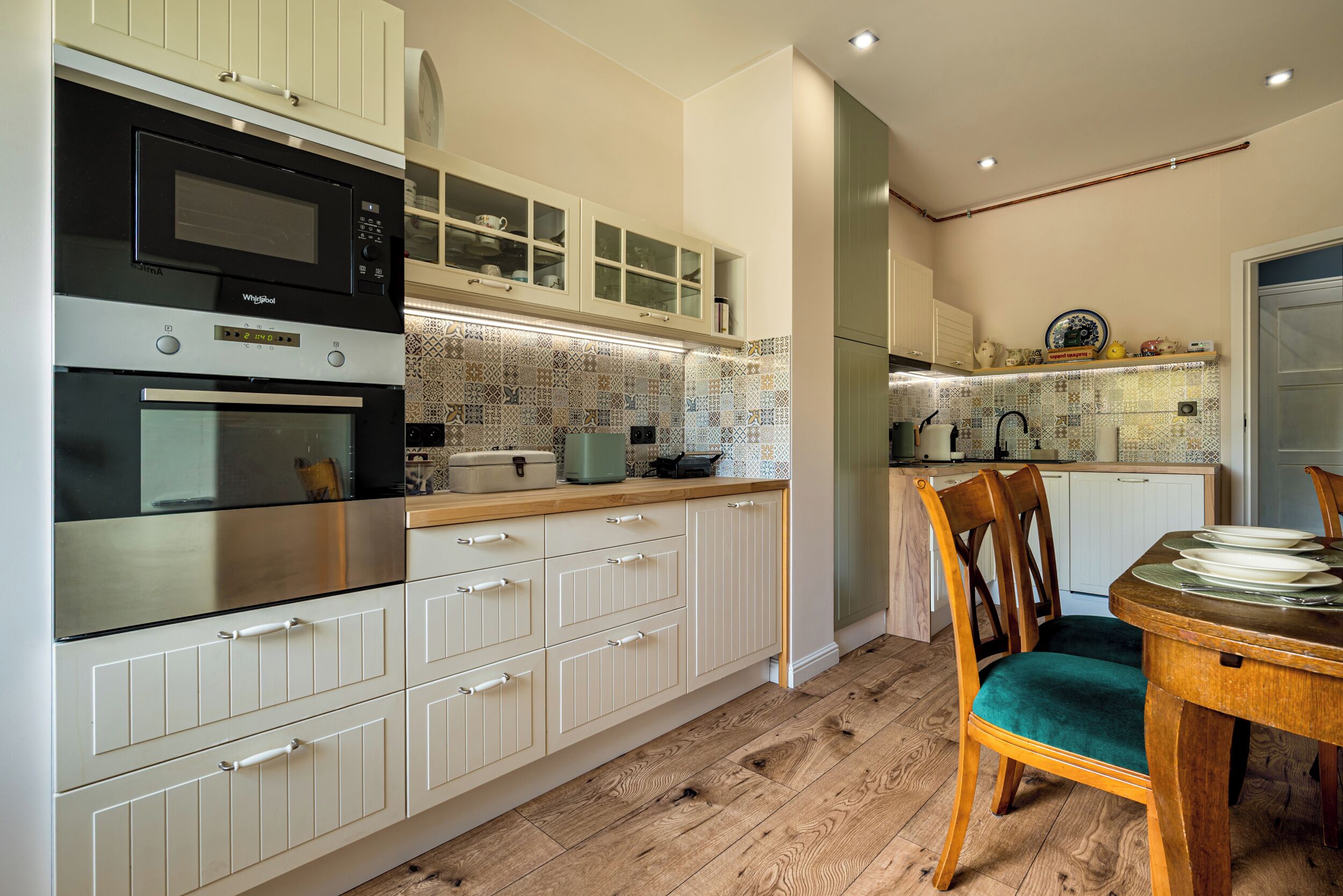 Una cocina con muebles blancos, microondas integrado, horno y mesa de comedor de madera con sillas.