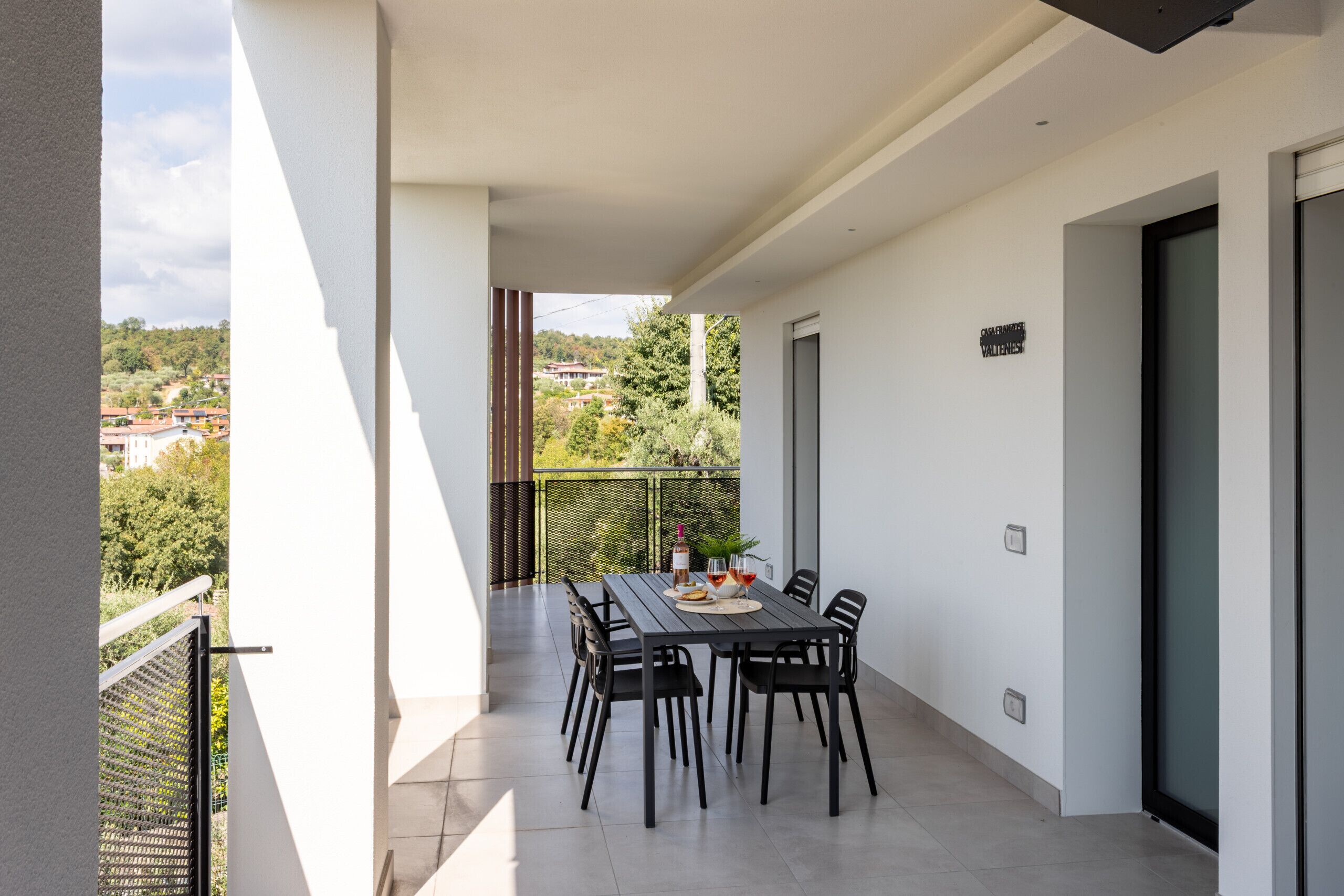 Un balcone con un tavolo apparecchiato per due persone, sedie e una bottiglia di vino.