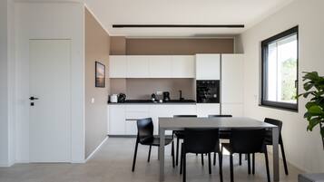 Una cucina moderna con mobili bianchi, un tavolo da pranzo con sedie e un'ampia finestra che lascia entrare luce naturale.