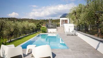 A swimming pool with lounge chairs, a covered patio area, and a view of a hilly landscape.