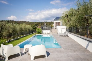 Ein Swimmingpool mit Liegestühlen, eine überdachte Terrasse und Blick auf eine hügelige Landschaft.