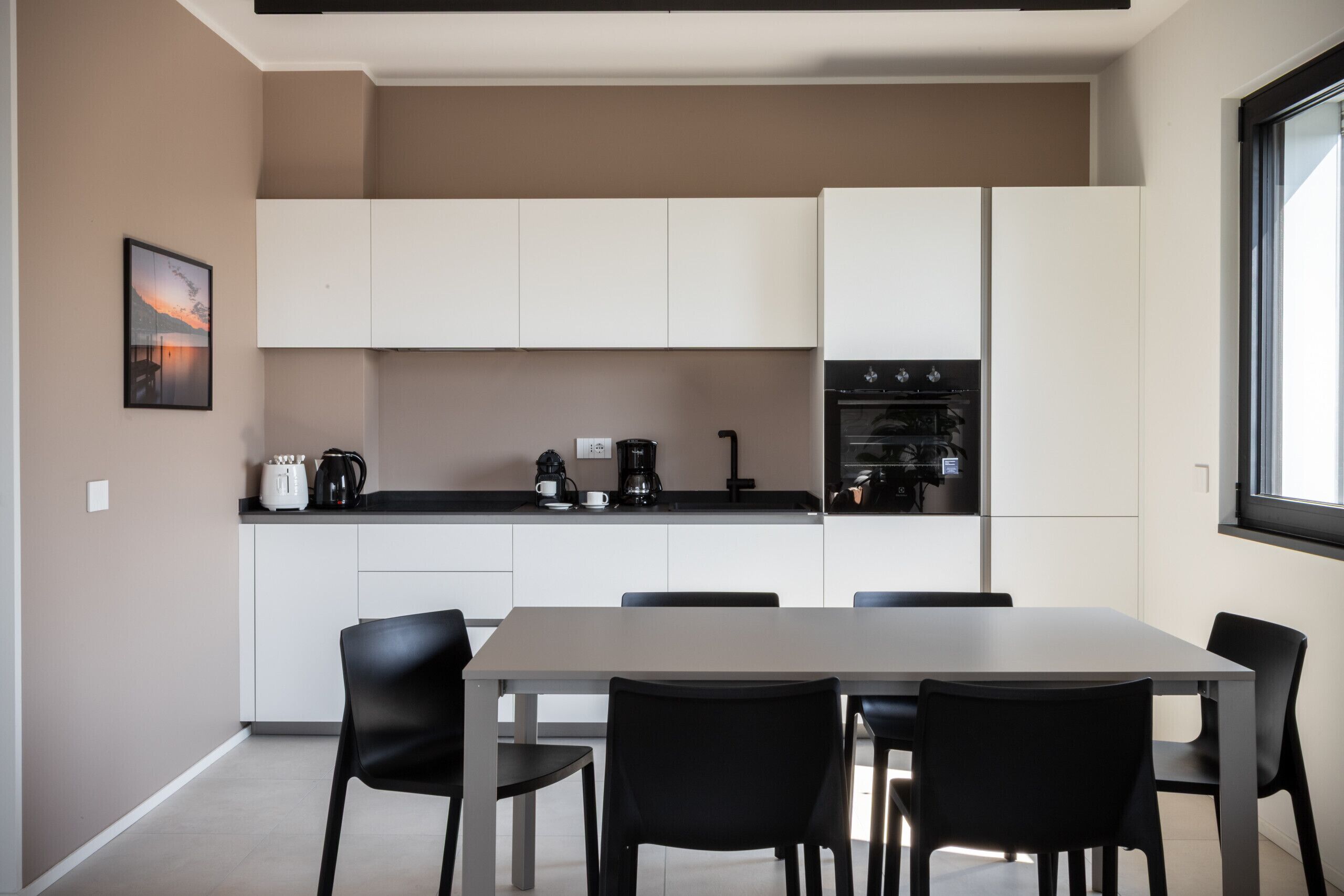 Une cuisine moderne avec des meubles blancs, une table à manger avec des chaises et une machine à café posée sur le plan de travail.