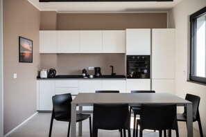 Eine moderne Küche mit weißen Schränken, einem Esstisch mit Stühlen und einer Kaffeemaschine auf der Arbeitsplatte.
