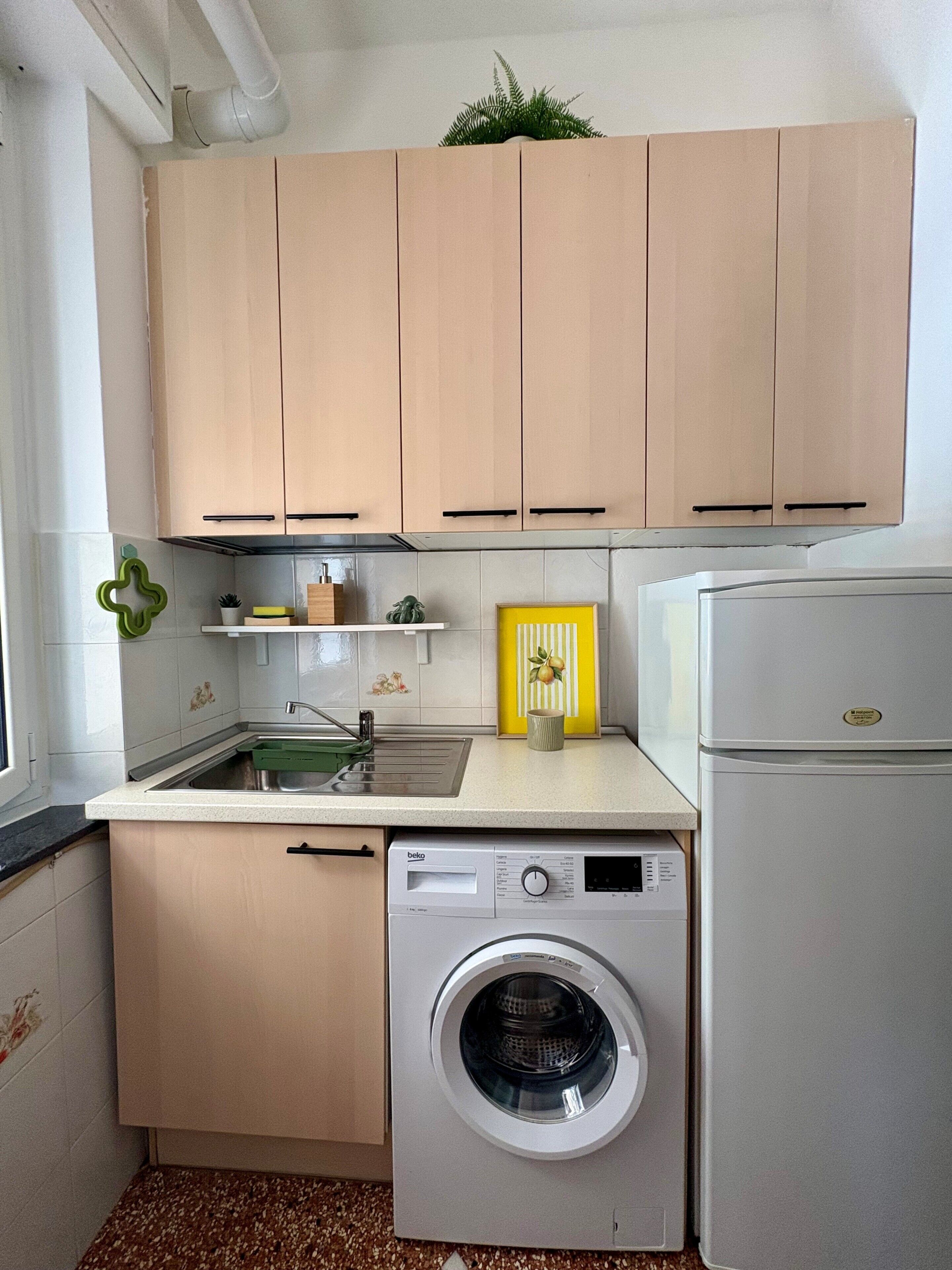 Eine kleine Küche mit Holzausstattung, einer integrierten Waschmaschine und einem Kühlschrank.