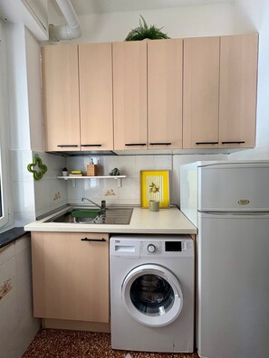 Eine kleine Küche mit Holzausstattung, einer integrierten Waschmaschine und einem Kühlschrank.