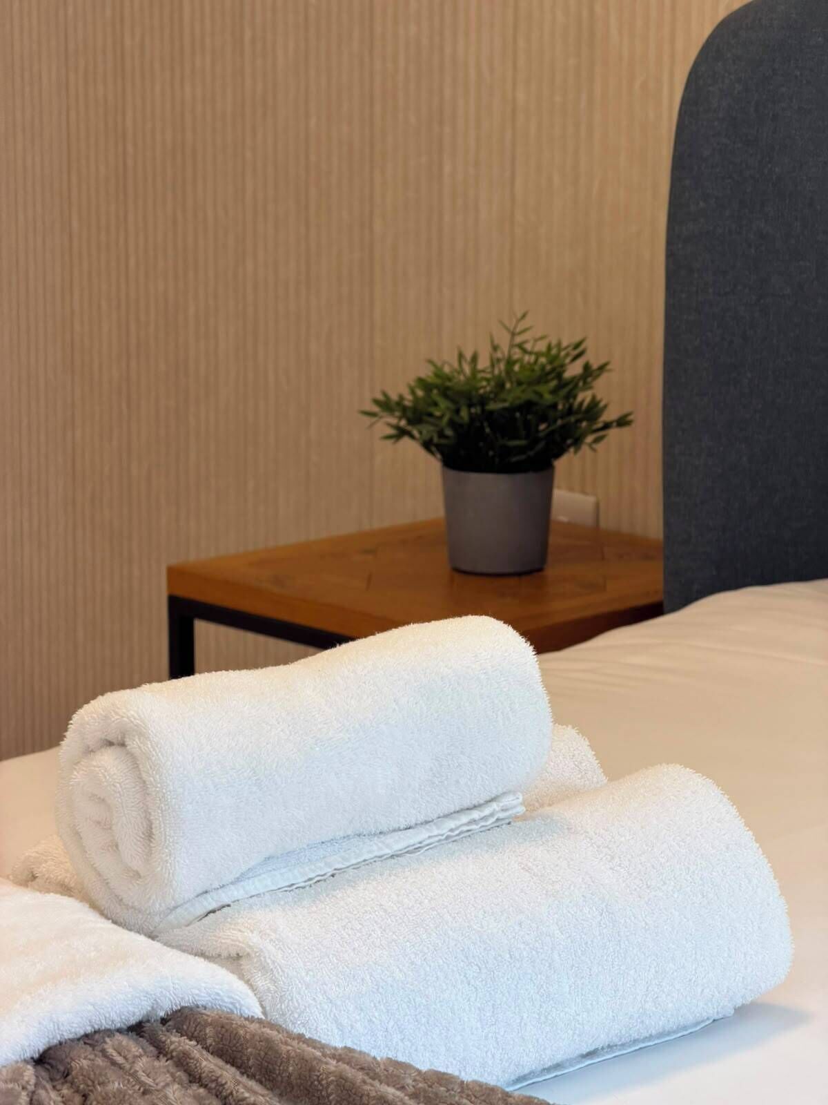 A neatly made bed with white towels and a potted plant on a wooden nightstand.