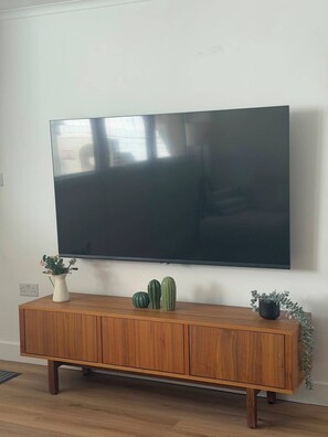 A flat-screen TV mounted on a wall above a wooden cabinet with three potted plants. - Chalk Farm- Camden 3 bedrooms Complex (London)