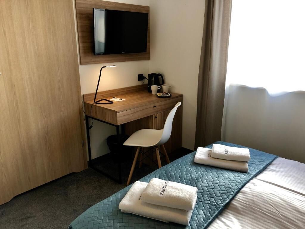 Una habitación de hotel con cama, escritorio, silla, televisor y ventana.