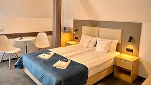 Una habitación de hotel con una cama, mesitas de noche, una silla y una pequeña mesa.