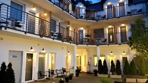 Un hotel de varios pisos con balcones, mobiliario exterior y plantas en macetas.