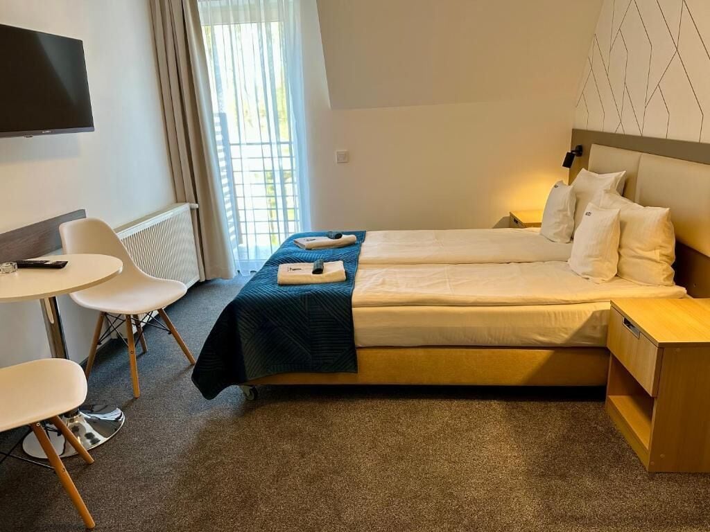 Habitación de hotel con cama, mesita de noche, silla y televisor montado en la pared.