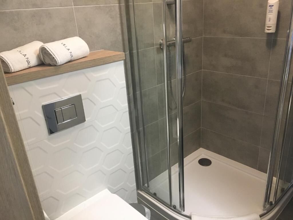 Eine Dusche mit Glastür, ein Handtuchhalter mit Handtüchern und ein an der Wand montierter Lichtschalter.