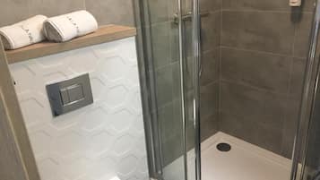 Eine Dusche mit Glastür, ein Handtuchhalter mit Handtüchern und ein an der Wand montierter Lichtschalter.