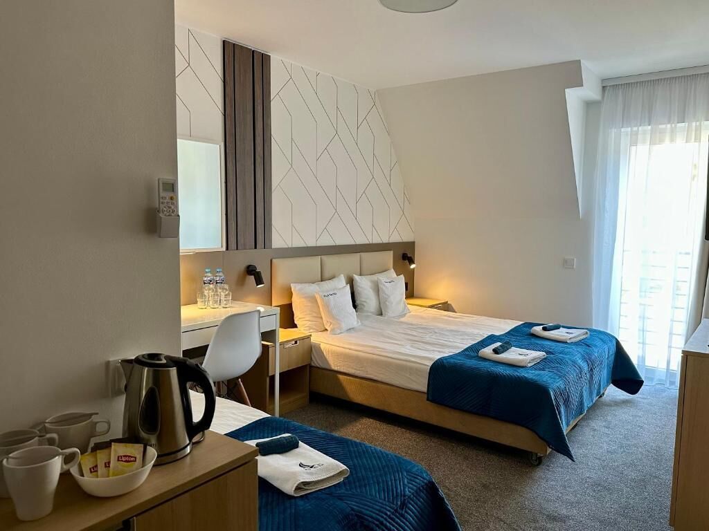 A hotel room with a bed, bedside tables, a desk, a chair, a coffee maker, and a window with curtains.