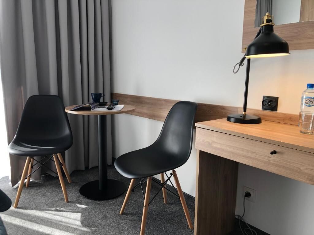 A hotel room with a desk, two chairs, a lamp, a water bottle, and a power outlet.
