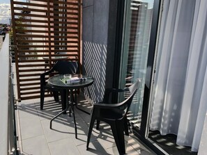 Un balcón con puerta de vidrio, una mesa redonda, dos sillas y un separador de madera con listones.