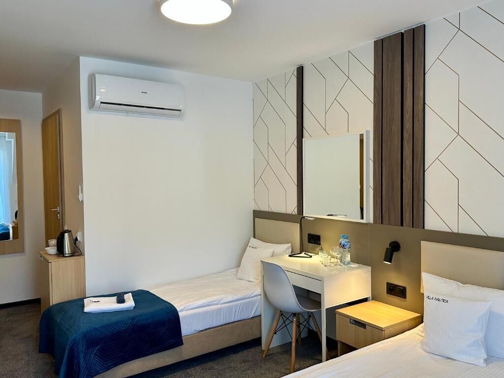 Una habitación de hotel con una cama, un escritorio, una silla, un equipo de aire acondicionado y un espejo.
