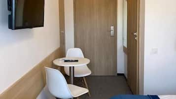 A hotel room with a bed, a TV mounted on the wall, a small table with two chairs, and a wooden door.