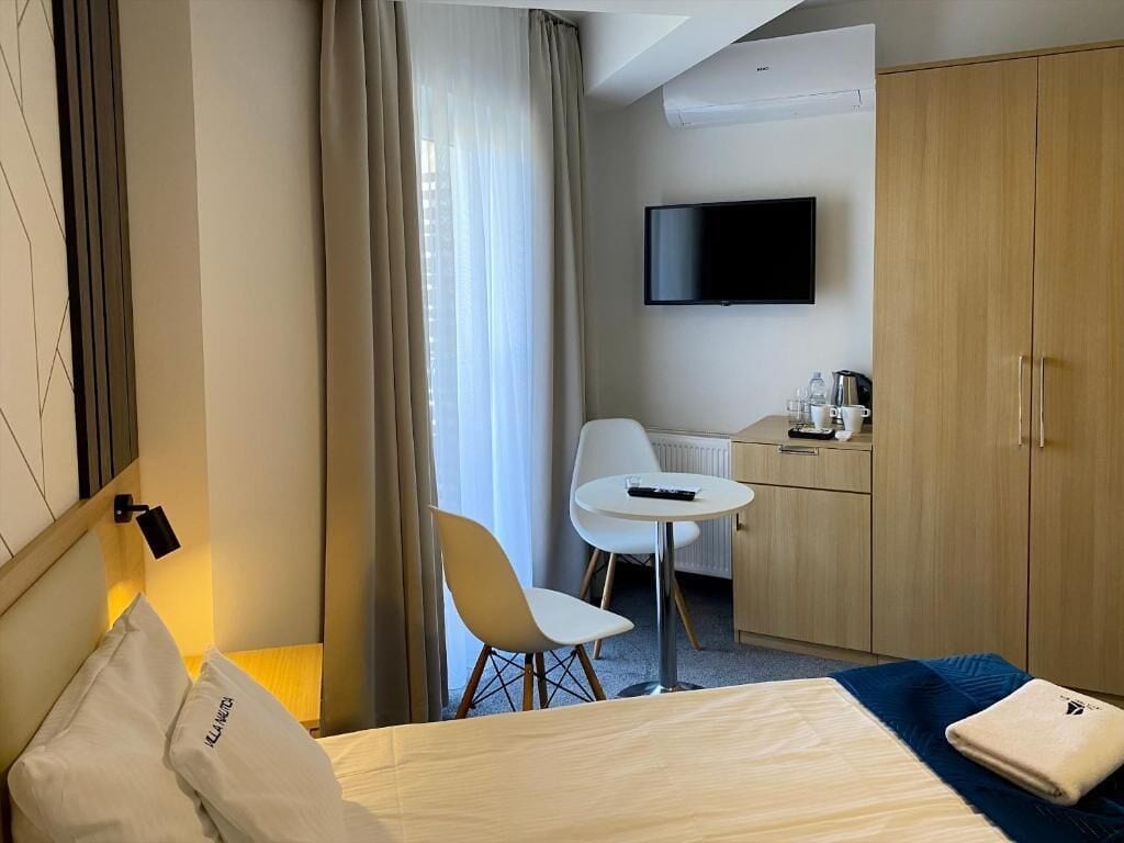 A hotel room with a bed, a desk, a chair, a television, and a wardrobe.