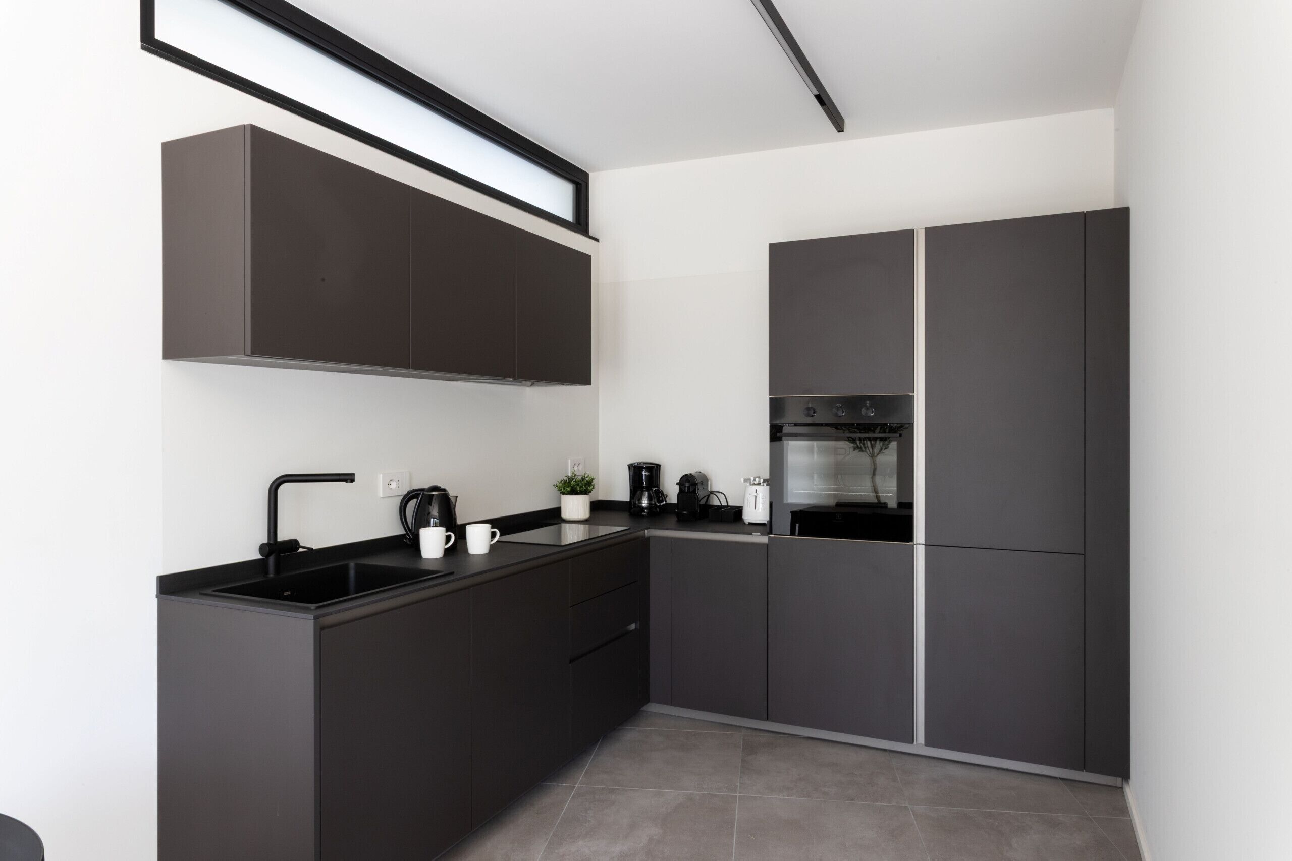 Une cuisine moderne avec des meubles de couleur sombre, un évier noir et un four encastré.