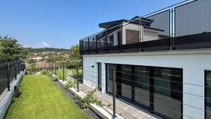 Un edificio moderno con techo plano, ventanas grandes y un balcón con barandilla de malla.