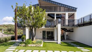 A modern two-story building with a balcony, a tree in the courtyard, and a clear sky.