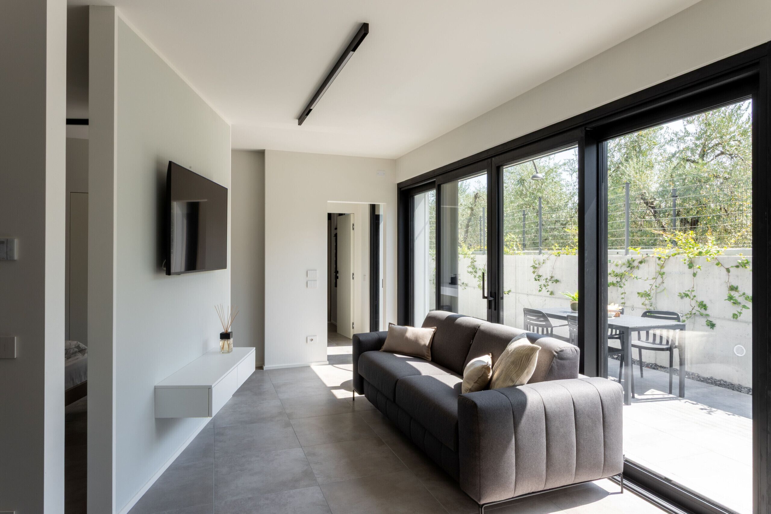 A modern living room with a sofa, a flat-screen TV, and large windows.