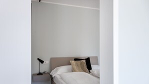 Un dormitorio minimalista con una cama individual, una mesita de noche con lámpara y un enchufe en la pared.