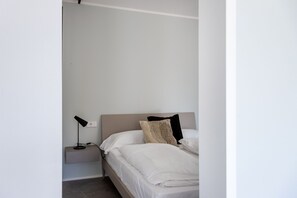 A minimalist bedroom with a single bed, a bedside table with a lamp, and a power outlet on the wall. - Casa Franzosi - Leccino Luxury (Puegnago sul Garda)